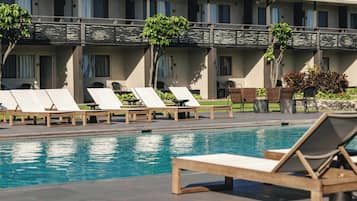 A pool area with lounge chairs and a building with multiple windows and balconies.