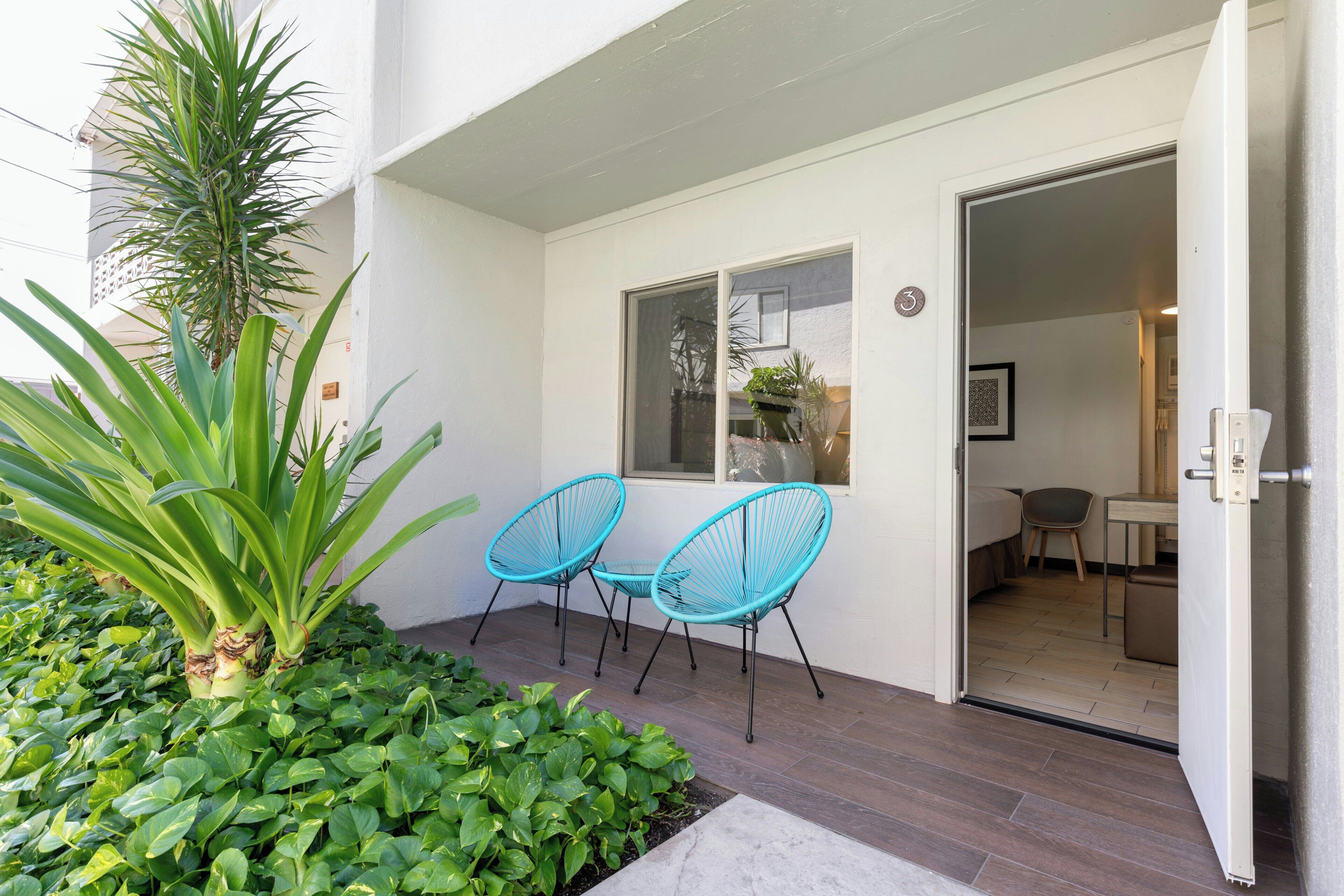A hotel entrance with a small outdoor seating area, a potted plant, and a door leading to a room.
