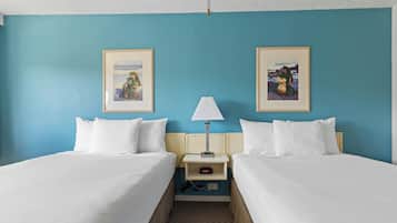 A hotel room with two beds, a nightstand with a lamp, and framed pictures on the walls.