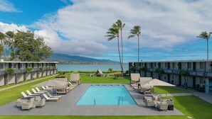 A pool area with lounge chairs and a view of the ocean.