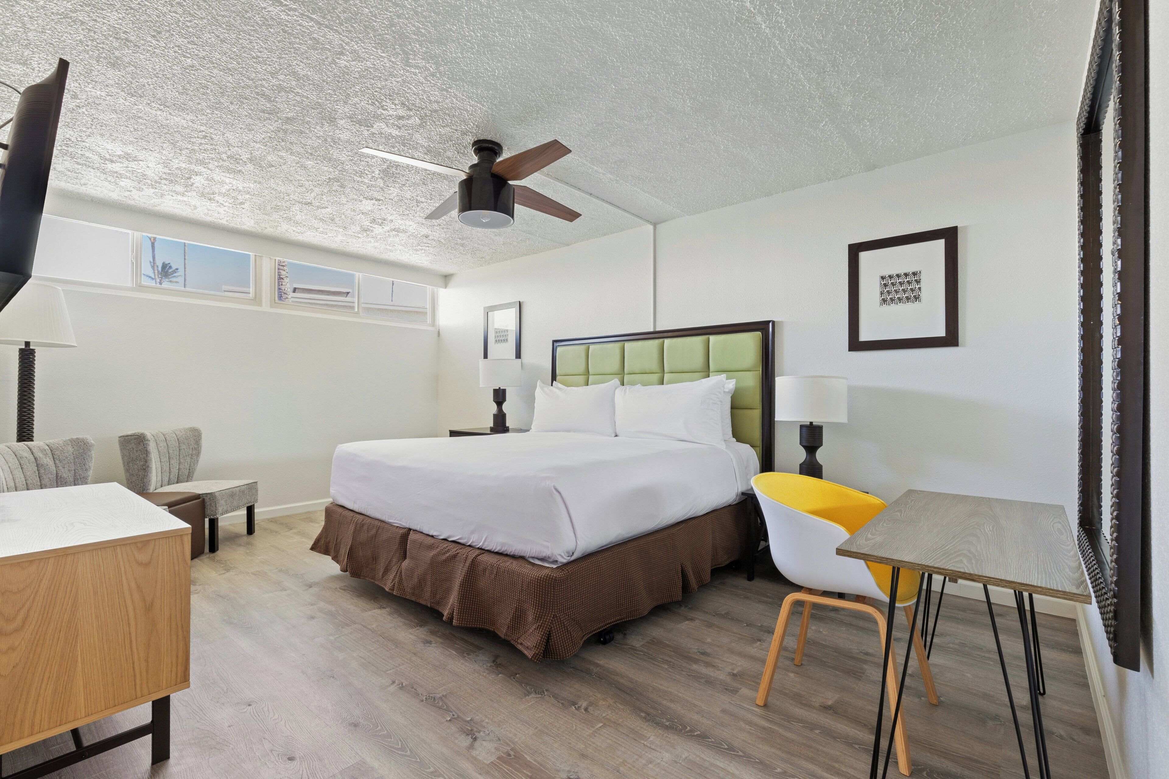 Habitación de hotel con cama, escritorio, silla, ventilador de techo y ventana.