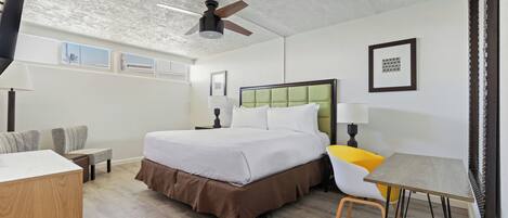 Habitación de hotel con cama, escritorio, silla, ventilador de techo y ventana.