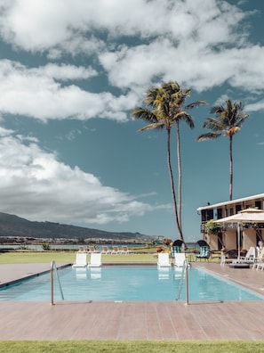A pool area with lounge chairs, palm trees, and a view of the mountains. - Maui Seaside Hotel (Kahului)
