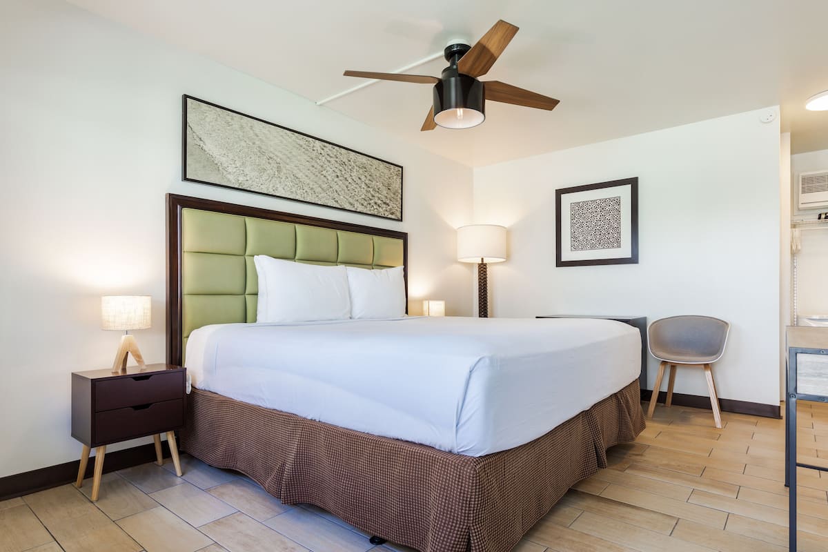 A hotel room with a large bed, a ceiling fan, a nightstand with a lamp, and a chair.