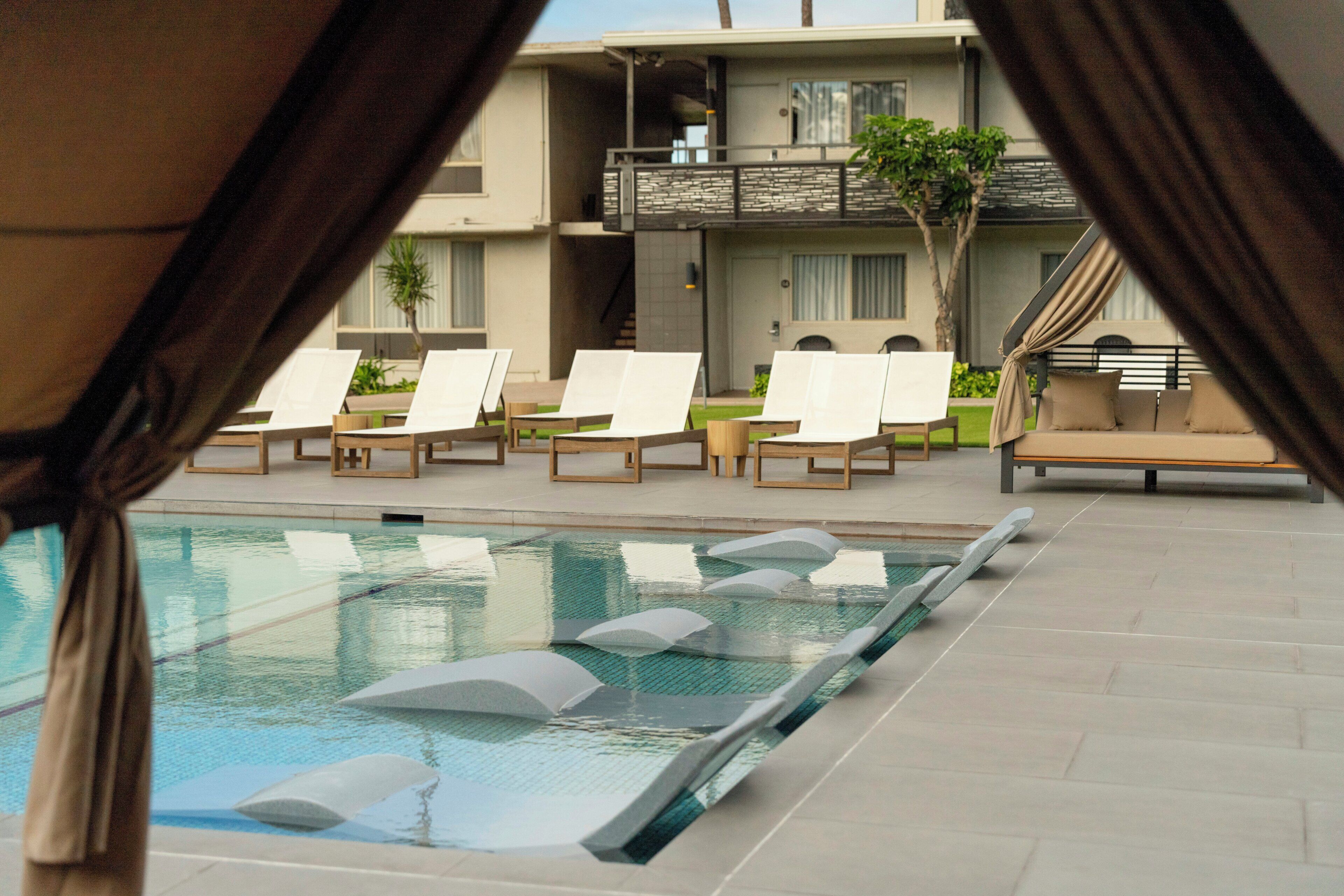 Un espace piscine avec des chaises longues, un canapé et un bâtiment doté d’un balcon.