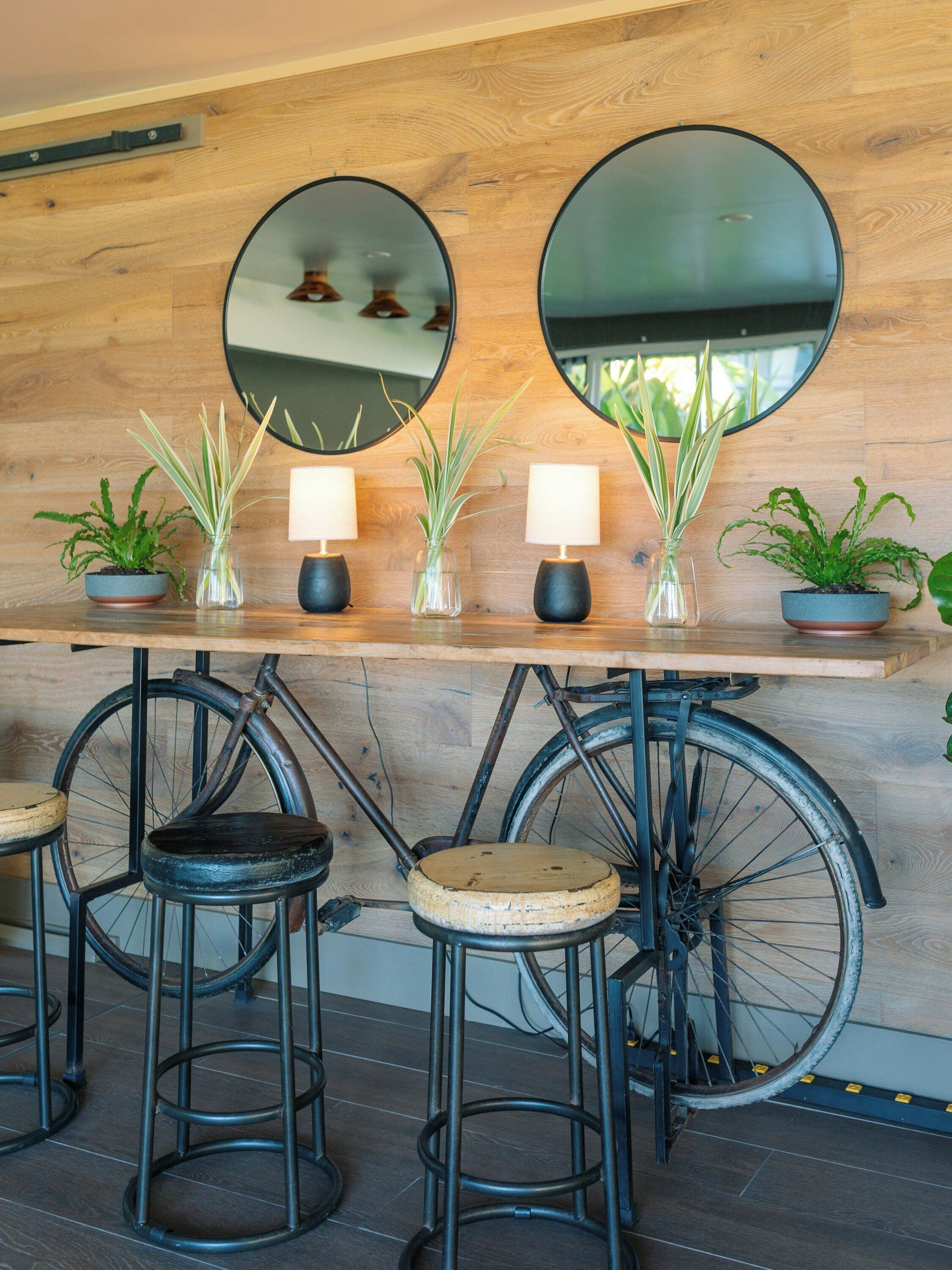 A wooden bar area with two round mirrors, potted plants, and stools.