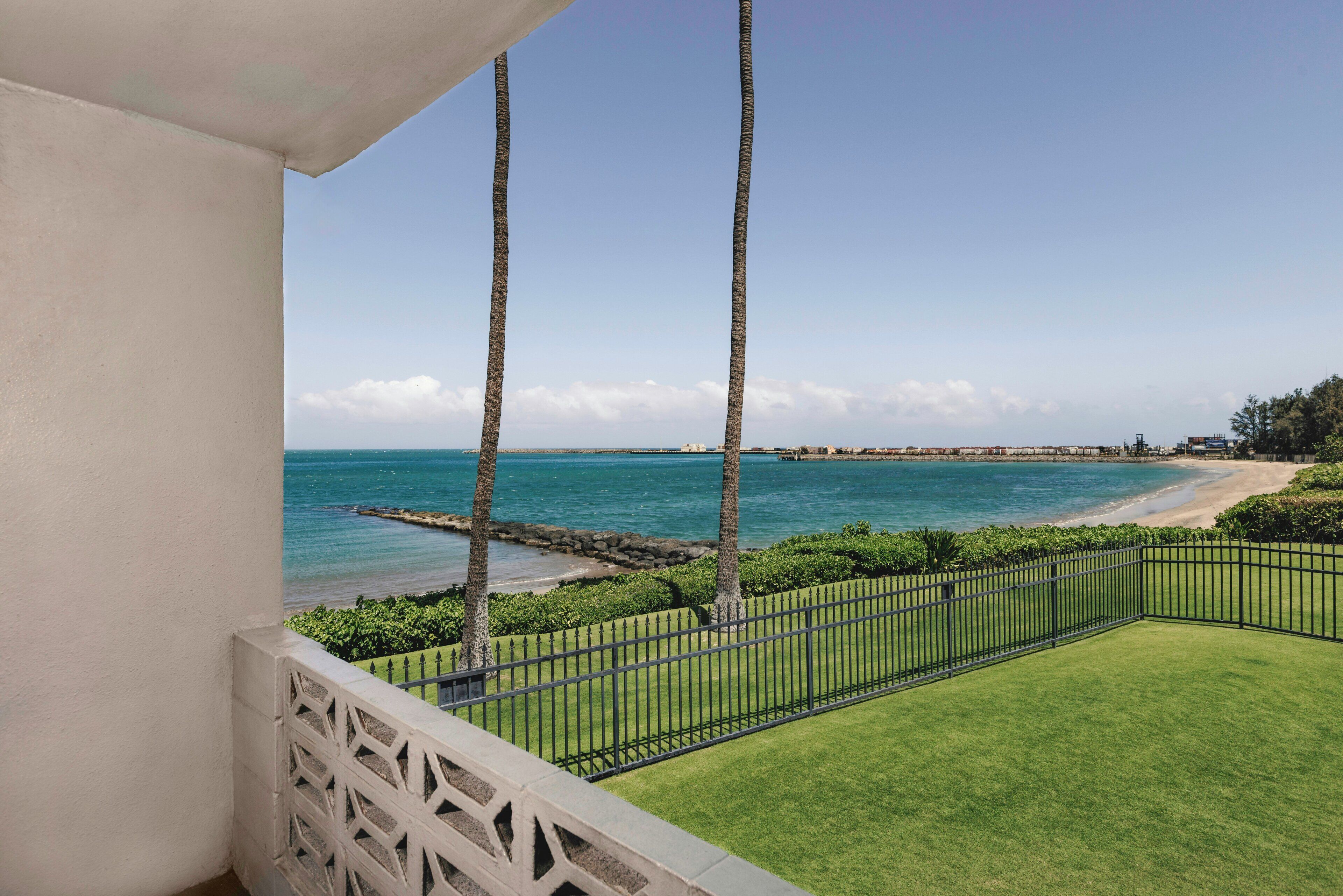 A balcony with a view of a beach, palm trees, and a clear sky.