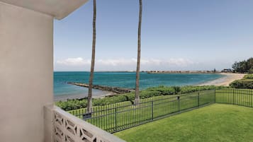 A balcony with a view of a beach, palm trees, and a clear sky.