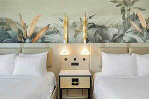 A hotel room with two beds, a nightstand with a drawer, wall-mounted lamps, and a tropical-themed mural. - Maui Seaside Hotel (Kahului)