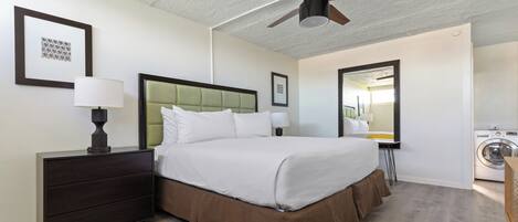 Habitación de hotel con cama, mesitas de noche, ventilador de techo, espejo y lavadora.