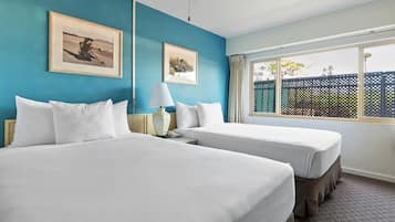 Une chambre d’hôtel avec deux lits, une fenêtre donnant sur une clôture et deux tableaux encadrés accrochés au mur.