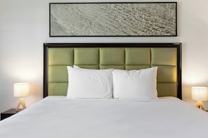 Habitación de hotel con cama, dos lámparas de noche, cabecera y un cuadro en la pared.