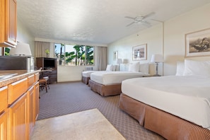 A hotel room with a large bed, a desk with a TV, and a view of palm trees. - Maui Seaside Hotel (Kahului)