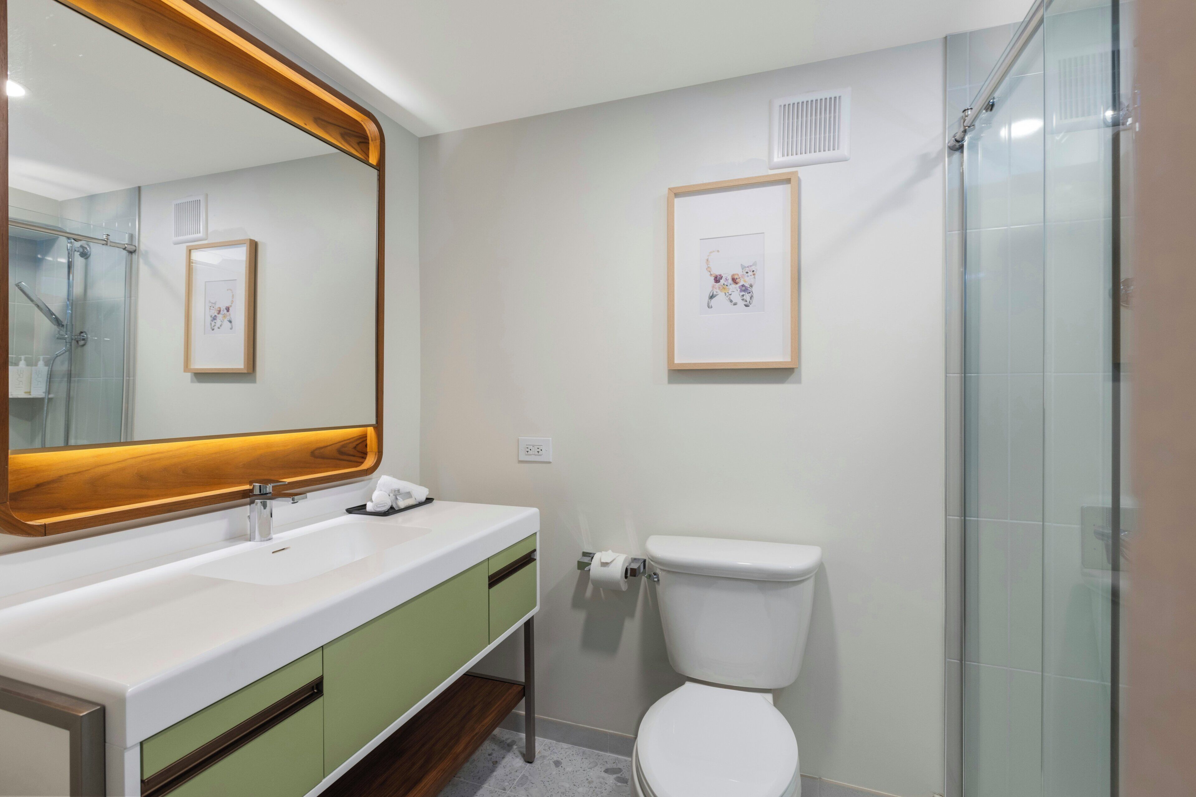 A modern bathroom with a large mirror, a white sink, a green vanity, and a glass shower enclosure.