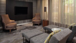 A modern living room with two armchairs, a sofa, a coffee table, and a flat-screen TV mounted on the wall. - Courtyard by Marriott Jacksonville at Mayo Clinic Campus/Beaches (Jacksonville)