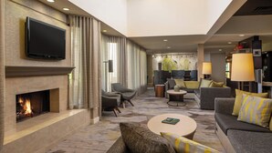 A modern hotel lobby with a flat-screen TV, a fireplace, comfortable seating, and a coffee bar. - Courtyard by Marriott Jacksonville at Mayo Clinic Campus/Beaches (Jacksonville)