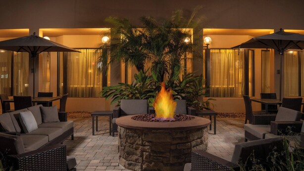 An outdoor seating area with stone fire pit, wicker furniture, and potted plants. - Courtyard by Marriott Jacksonville at Mayo Clinic Campus/Beaches (Jacksonville)