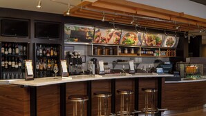 A bar area with a long counter, multiple stools, and shelves stocked with bottles. - Courtyard by Marriott Jacksonville at Mayo Clinic Campus/Beaches (Jacksonville)