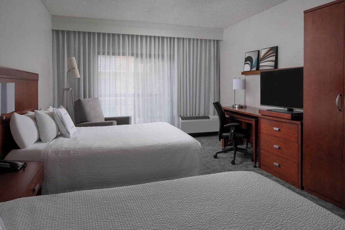 Une chambre d’hôtel avec deux lits, un bureau, une télévision et une armoire.