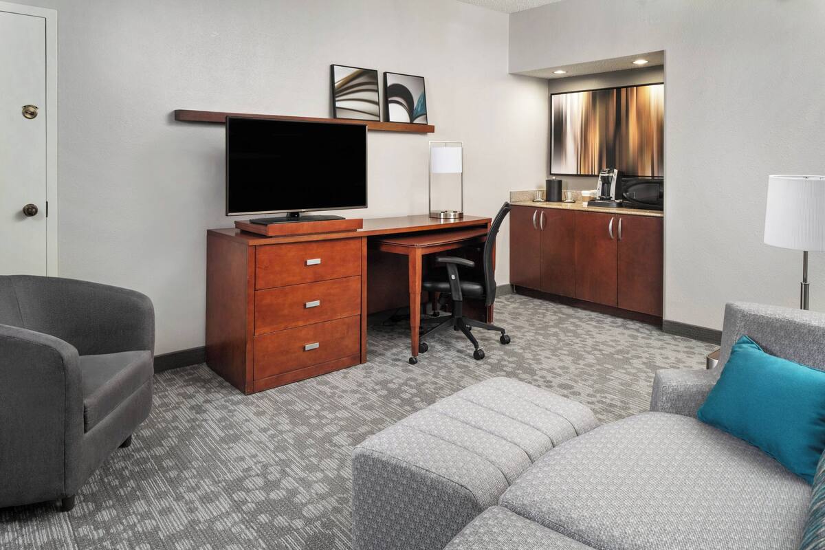Une chambre d’hôtel équipée d’un bureau, d’une télévision, d’un canapé, d’une chaise et d’une kitchenette.