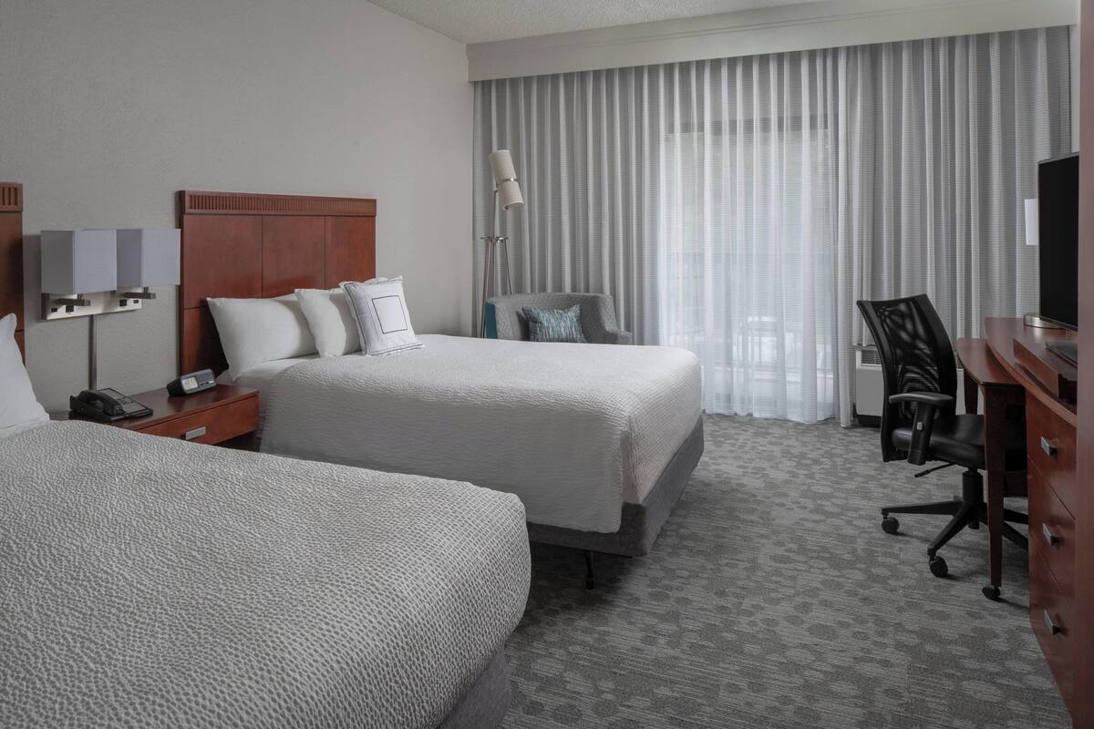 Une chambre d’hôtel avec deux lits, un bureau, une chaise, une lampe et un téléviseur.