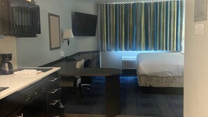 Ein Hotelzimmer mit Bett, Schreibtisch mit Stuhl, Wandfernseher und einem Fenster mit Vorhängen.
