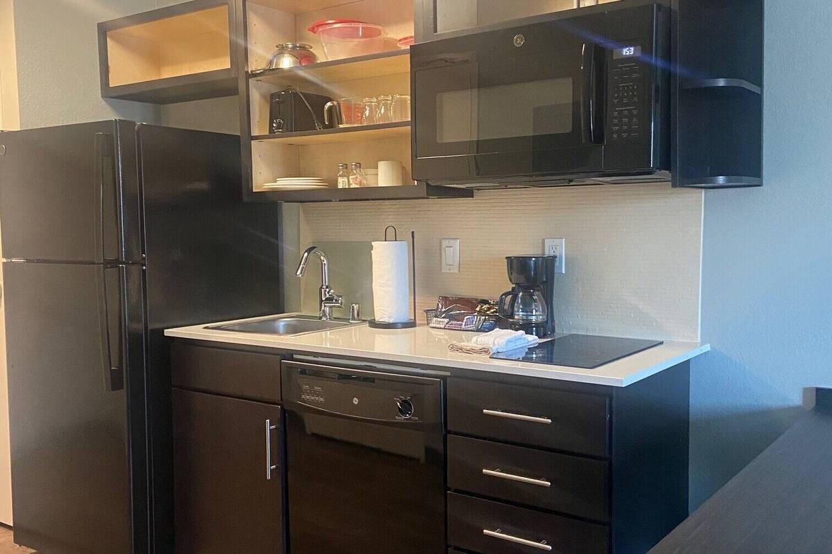 Una cocina compacta con un refrigerador negro, un microondas y un lavamanos.