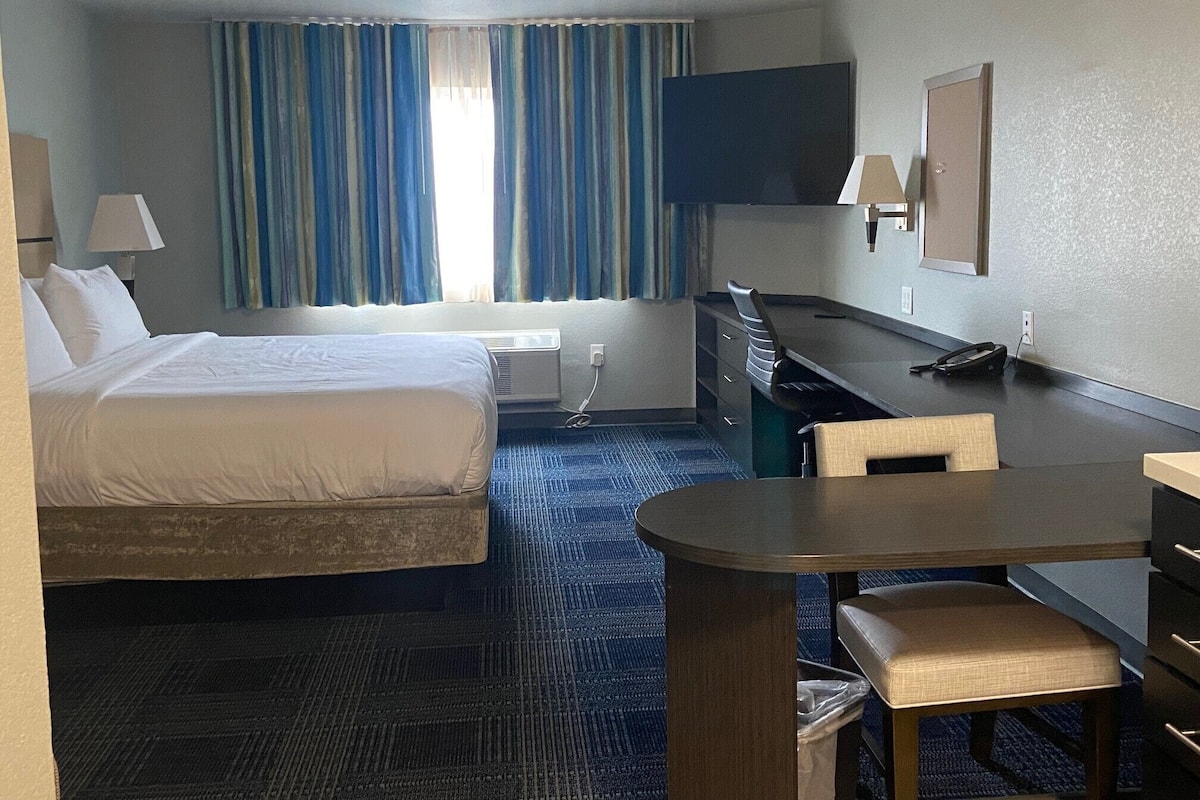 Una habitación de hotel con cama, escritorio, silla, televisor y ventana con cortinas.