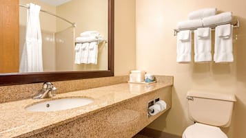 A bathroom with a granite countertop sink, a mirror, a towel rack with folded towels, and a toilet.