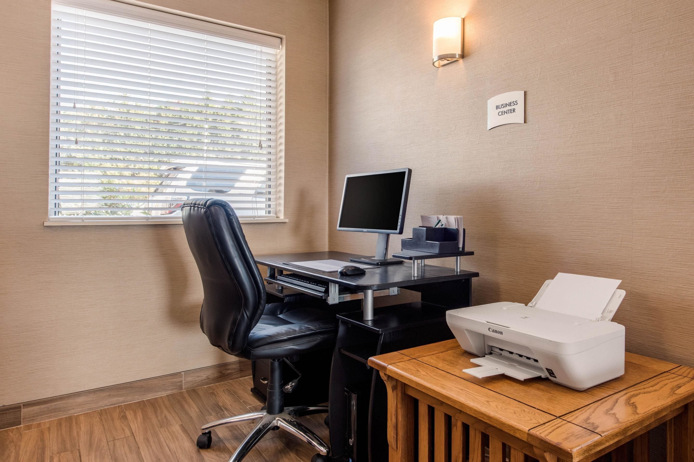 A business center with a desk, computer, printer, and a sign indicating the location.