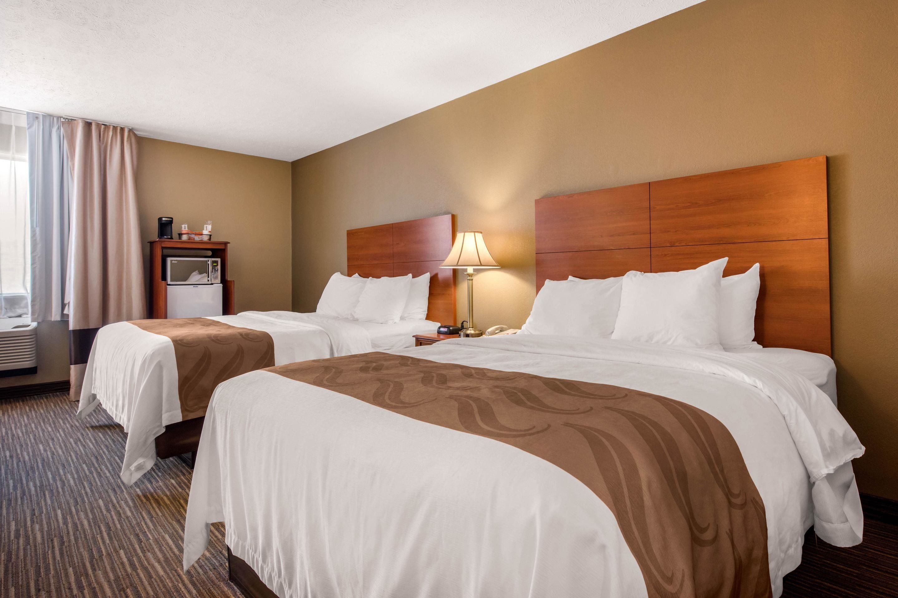 Quarto de hotel com duas camas, minibar, luminária e janela com cortinas.