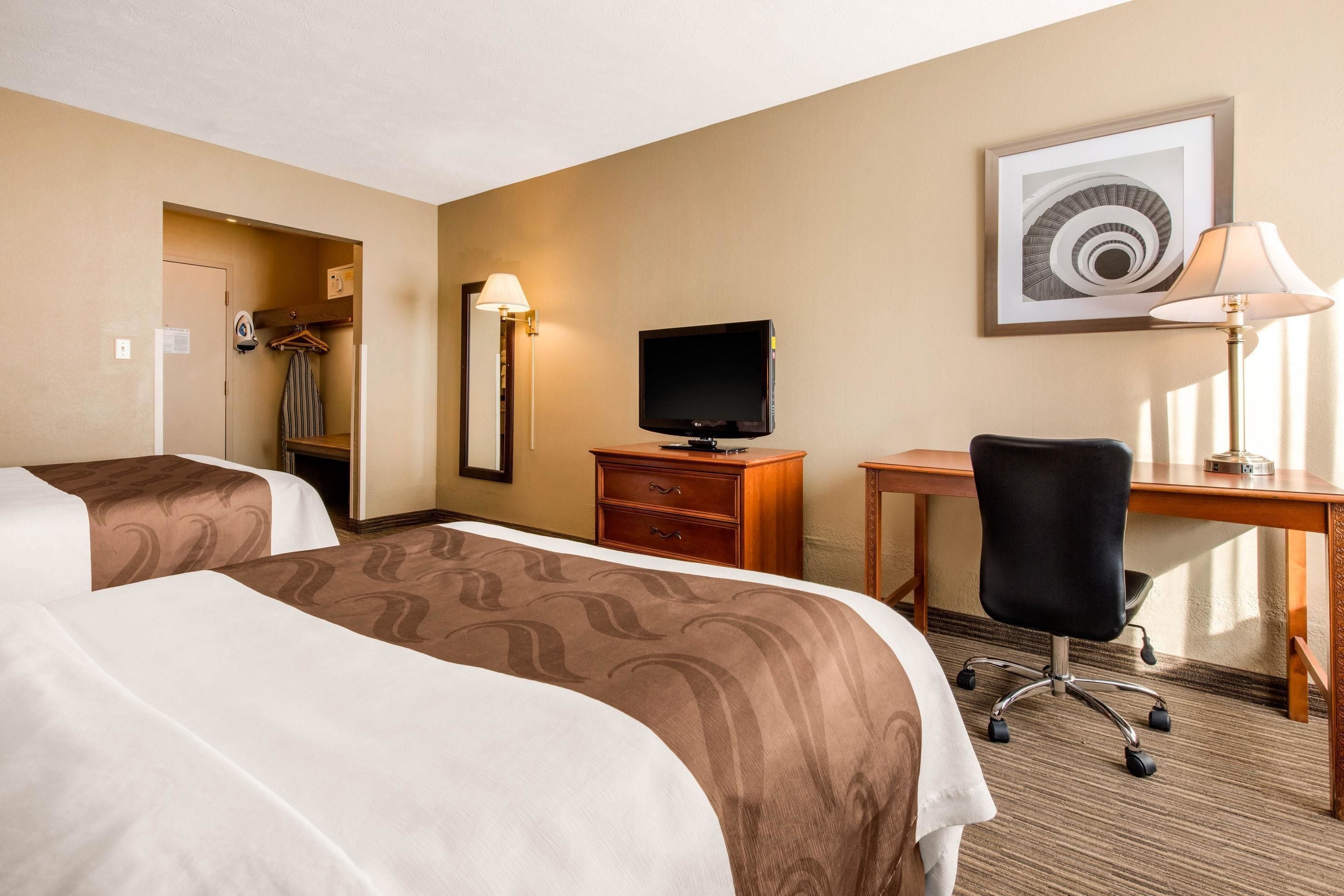 A hotel room with two beds, a desk, a chair, a television, and a lamp.