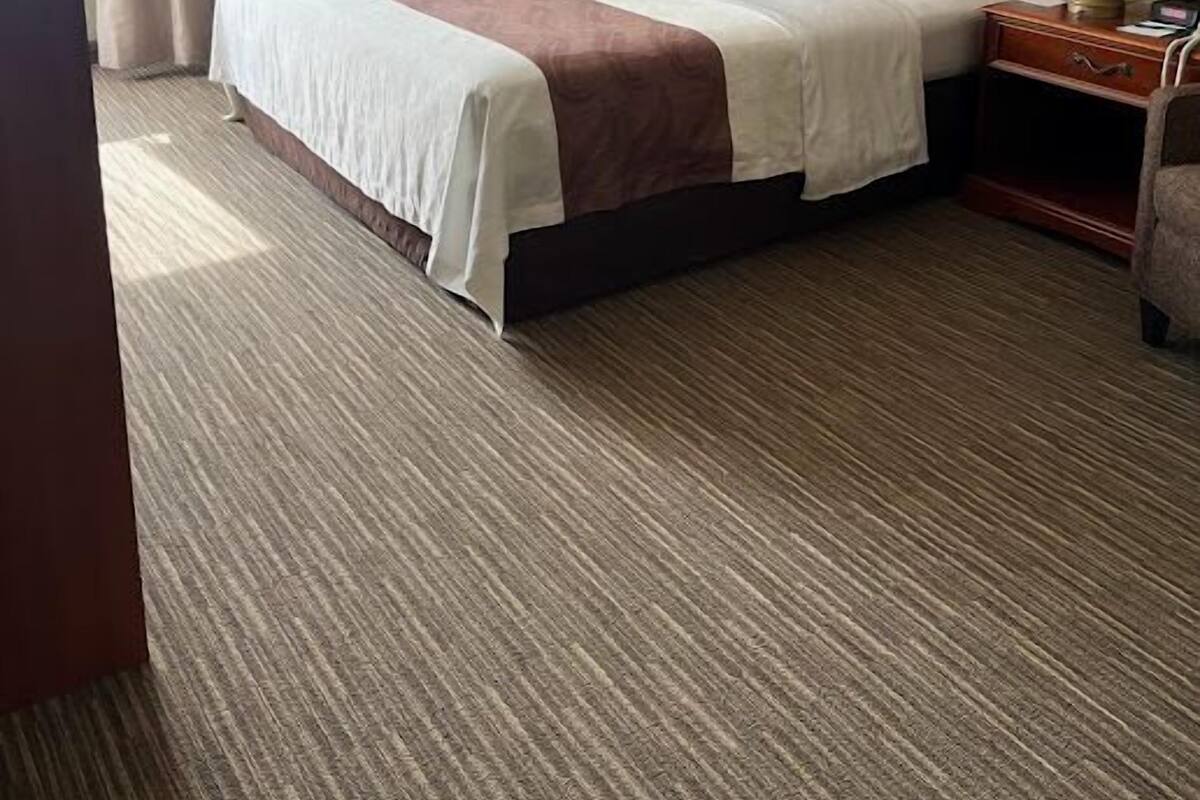 A hotel room with a large bed, a wooden headboard, a nightstand with a lamp, and a window with curtains.