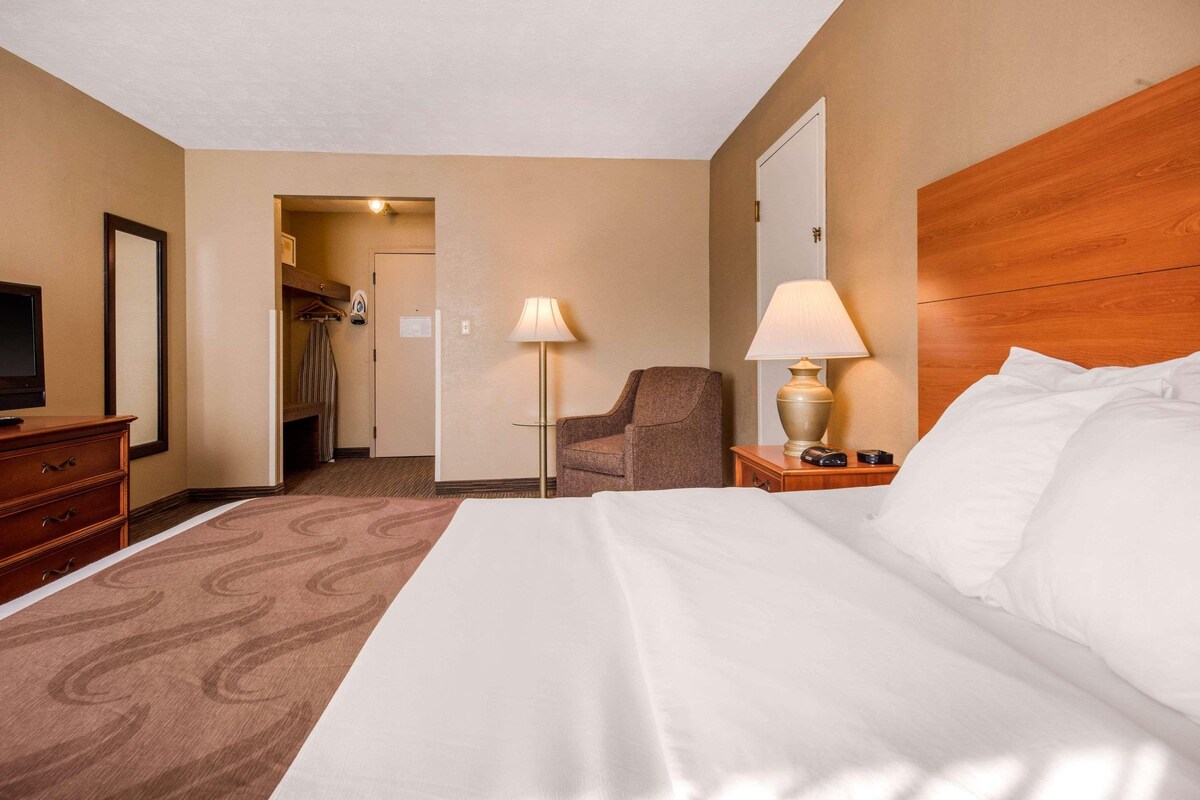 Quarto de hotel com cama, escrivaninha, cadeira, televisão e guarda-roupa.