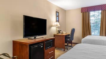 Et hotelværelse med et fladskærms-tv, et skrivebord med lampe, en mikrobølgeovn, en stol og to senge.