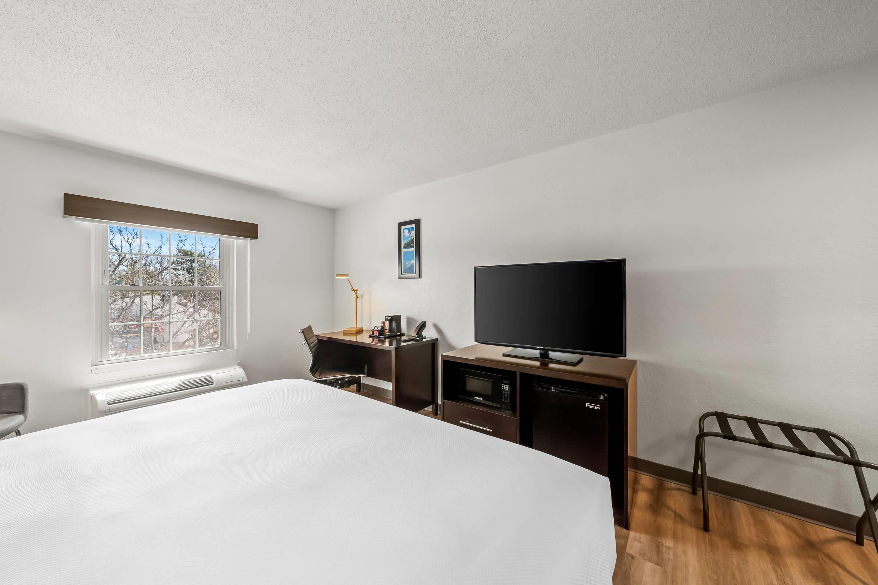 A hotel room with a bed, a desk with a computer, a television, and a window.