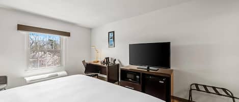 A hotel room with a bed, a desk with a computer, a television, and a window.