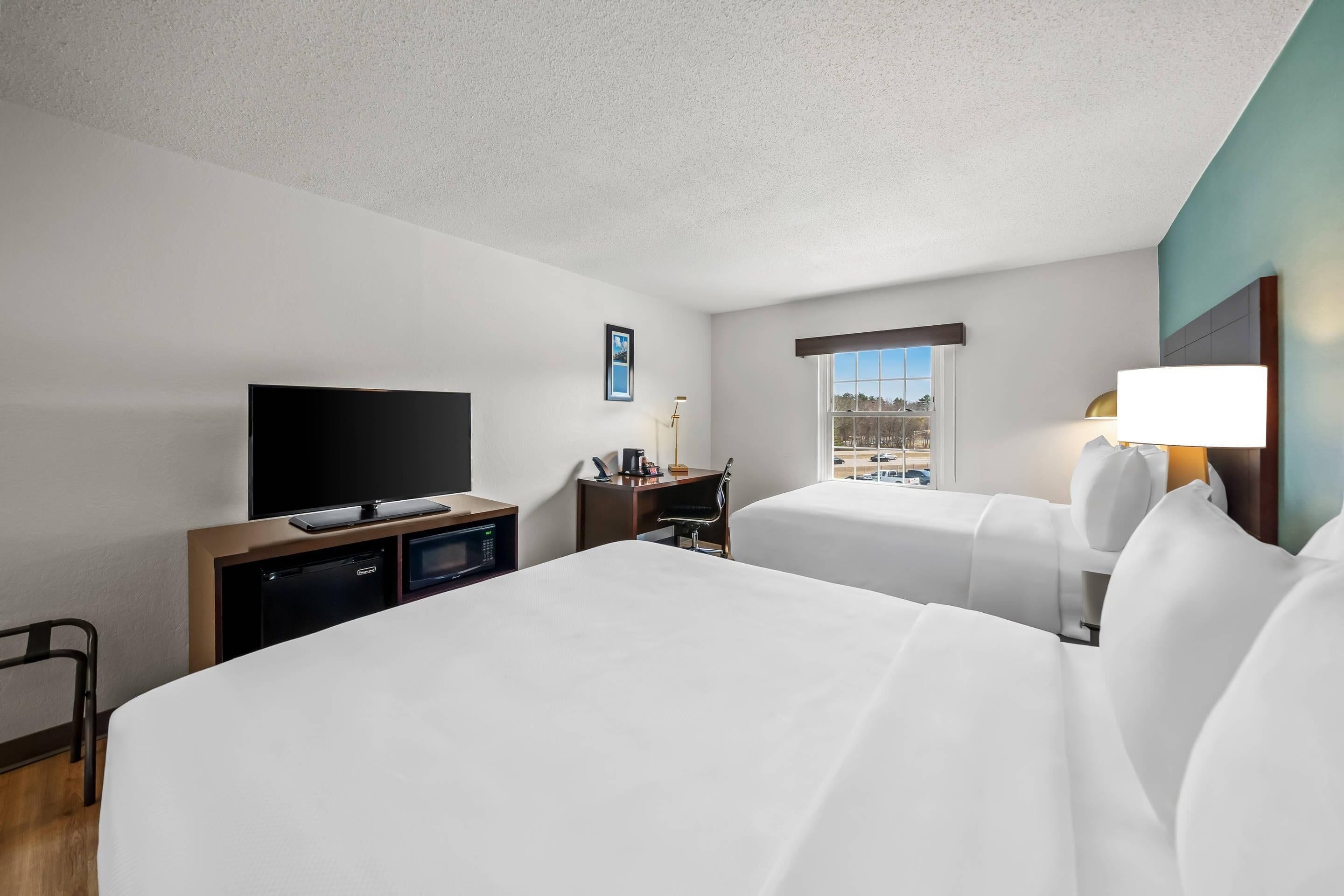 A hotel room with two beds, a TV, a desk with a lamp, and a window with a view.