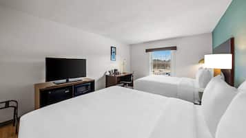 A hotel room with two beds, a TV, a desk with a lamp, and a window with a view.