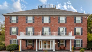 A two-story brick building with a balcony, a front door, and two windows on the ground floor.