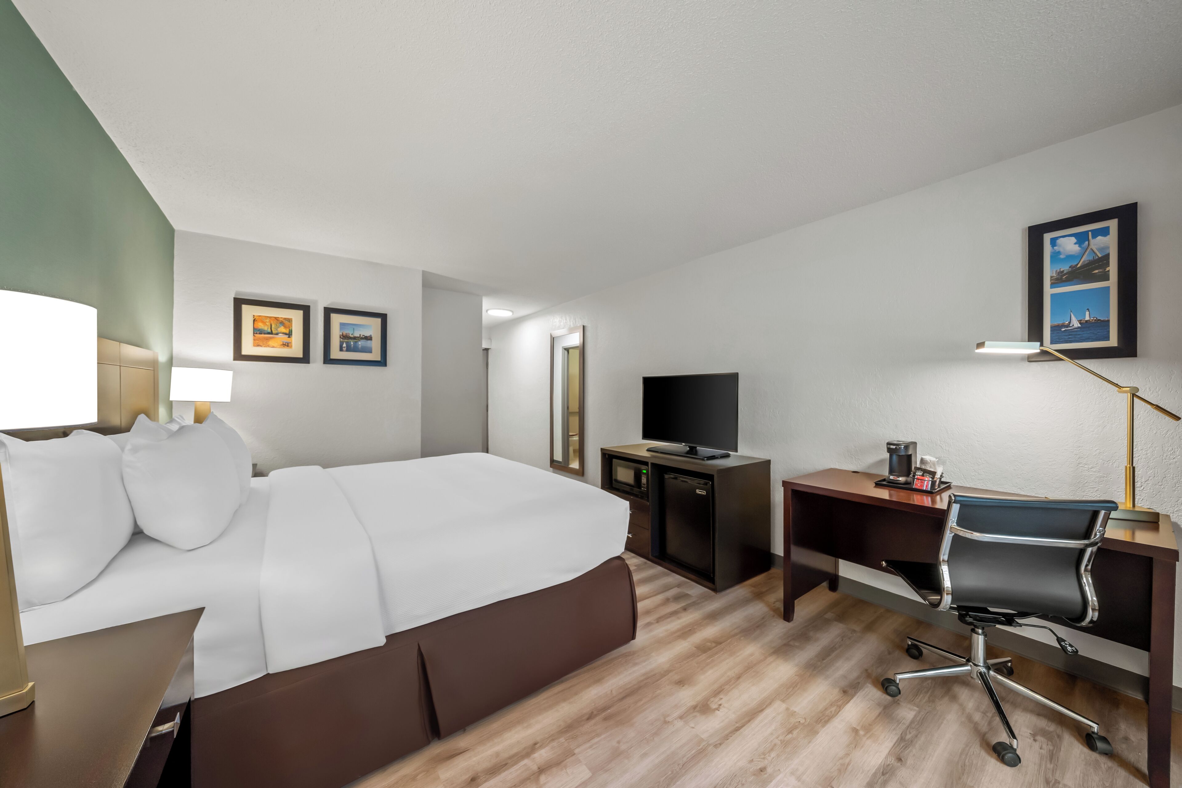 A hotel room with a bed, desk, chair, TV, and artwork on the walls.