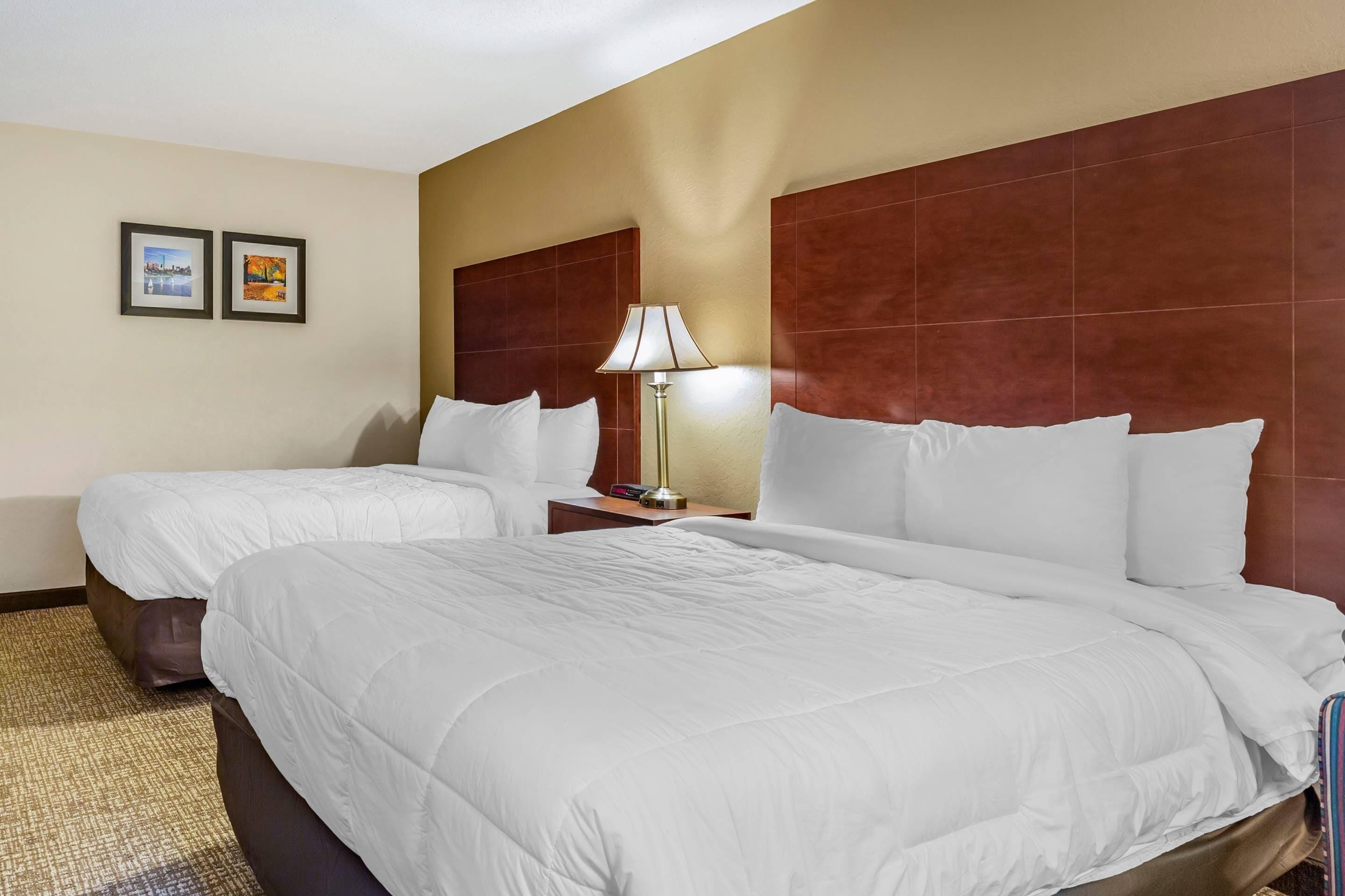 A hotel room with two beds, a nightstand with a lamp, and two framed pictures on the wall.