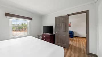 A bedroom with a bed, a dresser, a television, and a door leading to another room.