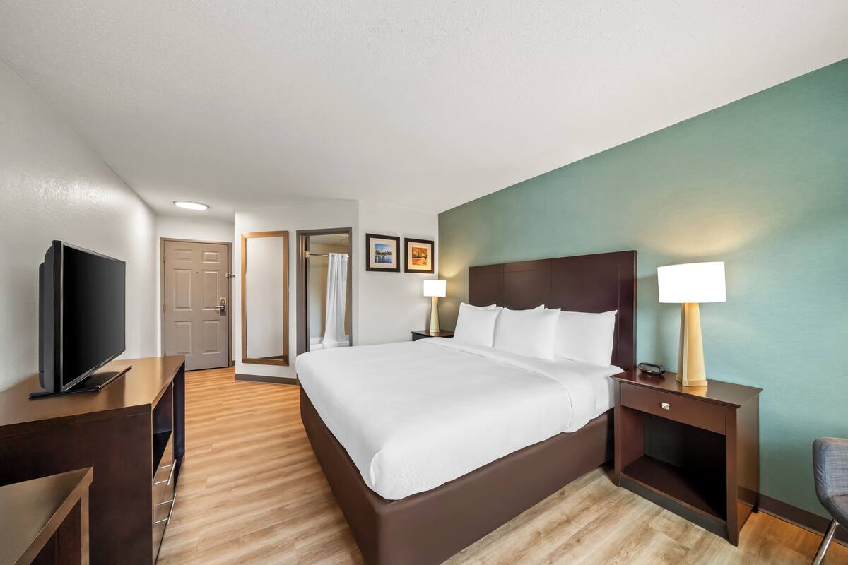 Une chambre d’hôtel comprenant un lit, des tables de chevet, une télévision et une porte donnant accès à une salle de bain.