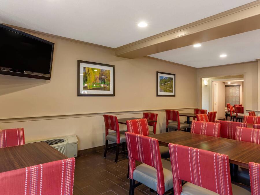 A conference room with a flat-screen TV, framed pictures, red upholstered chairs, and a wooden table.