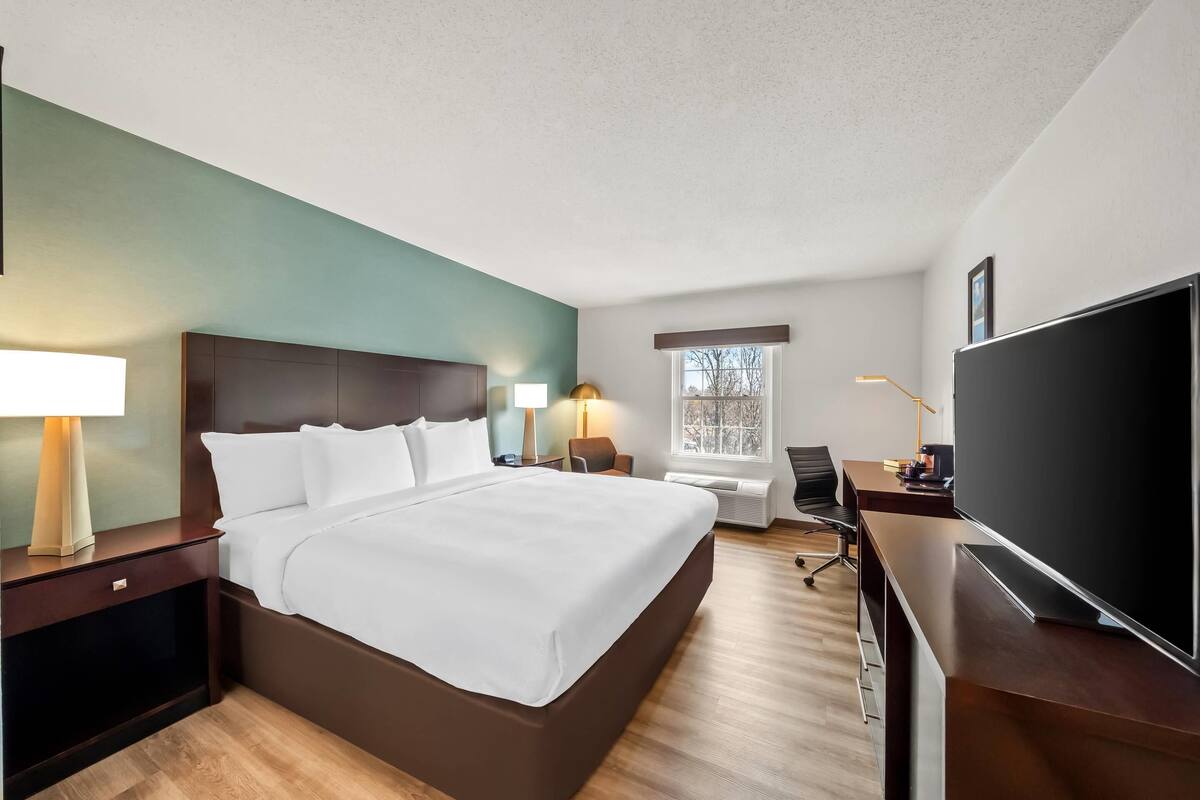 Une chambre d’hôtel avec un lit, des tables de chevet, un bureau avec une télévision, une chaise et une fenêtre.