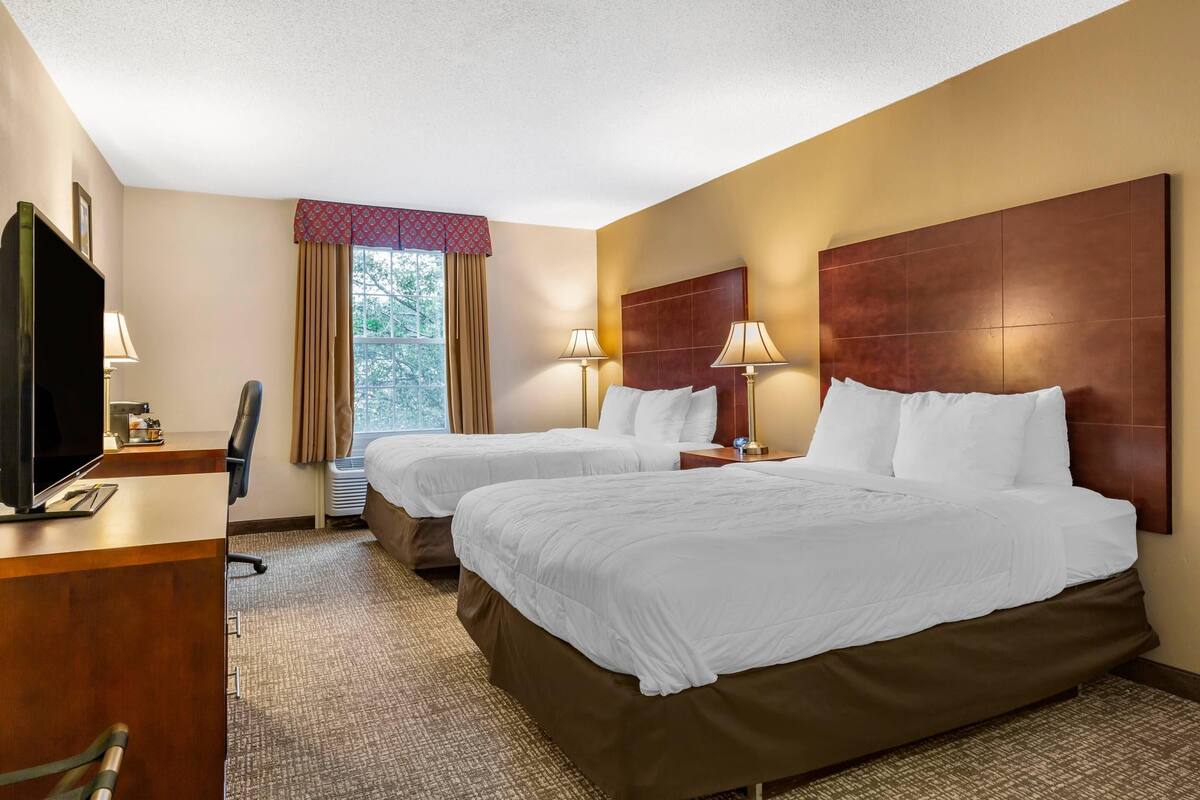 Une chambre d’hôtel avec deux lits, un bureau avec une télévision et une fenêtre avec des rideaux.