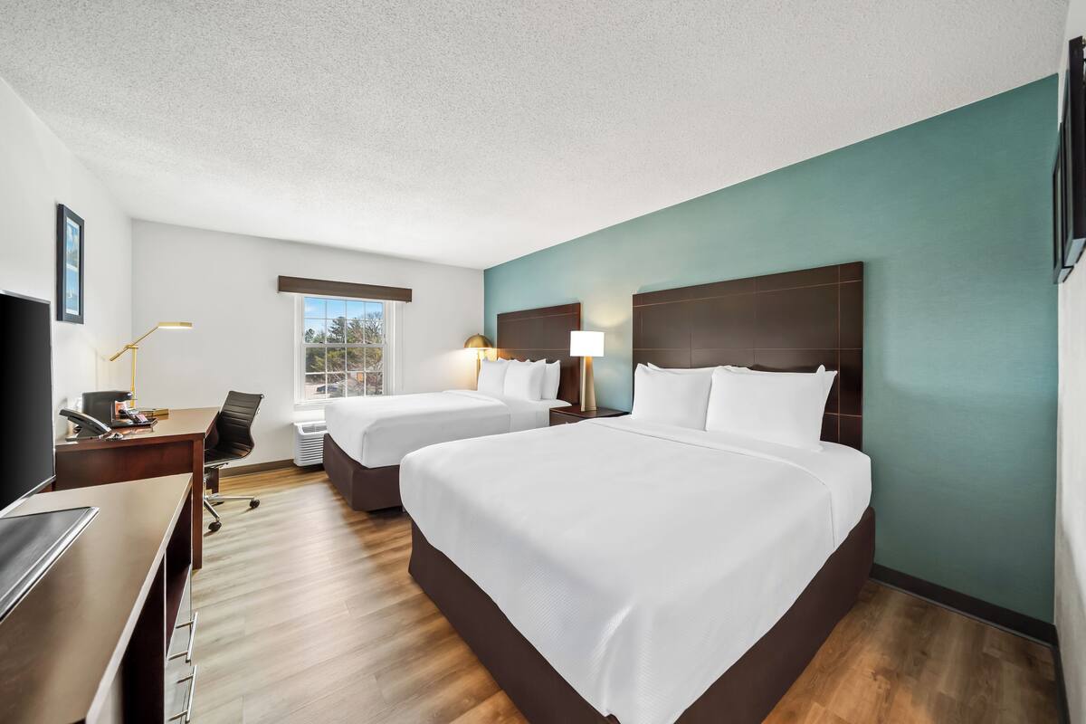 Une chambre d’hôtel avec deux lits, un bureau, une chaise, une télévision et une fenêtre.