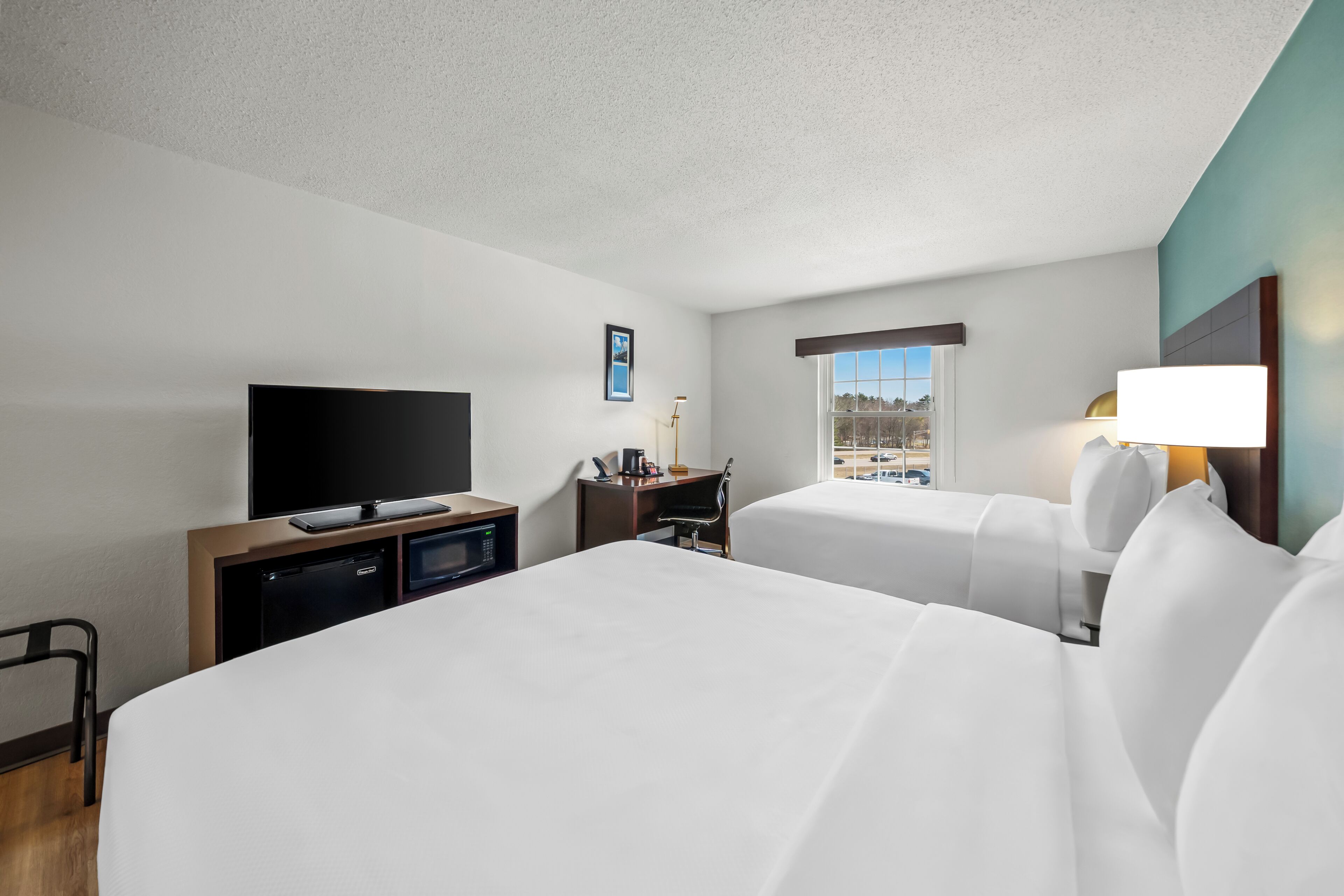 Habitación de hotel con dos camas, televisión, escritorio con lámpara y ventana con vista.