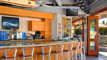 A bar area with wooden bar stools, a counter with a cash register, and surfboards mounted on the ceiling.